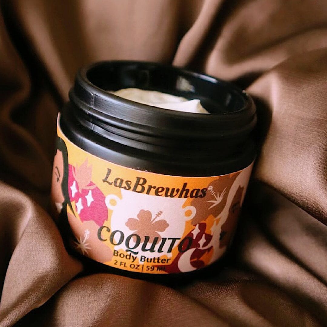 Las Brewhas Coquito body butter, with its illustrated label, on brown fabric
